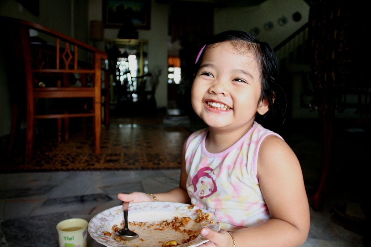 A young girl smiling holding an empty plate, sitting on the ground