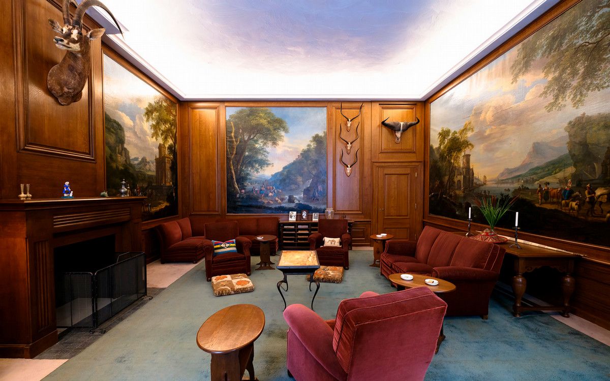 A large, comfortable looking room with plush armchairs, large paintings, and mounted animal heads