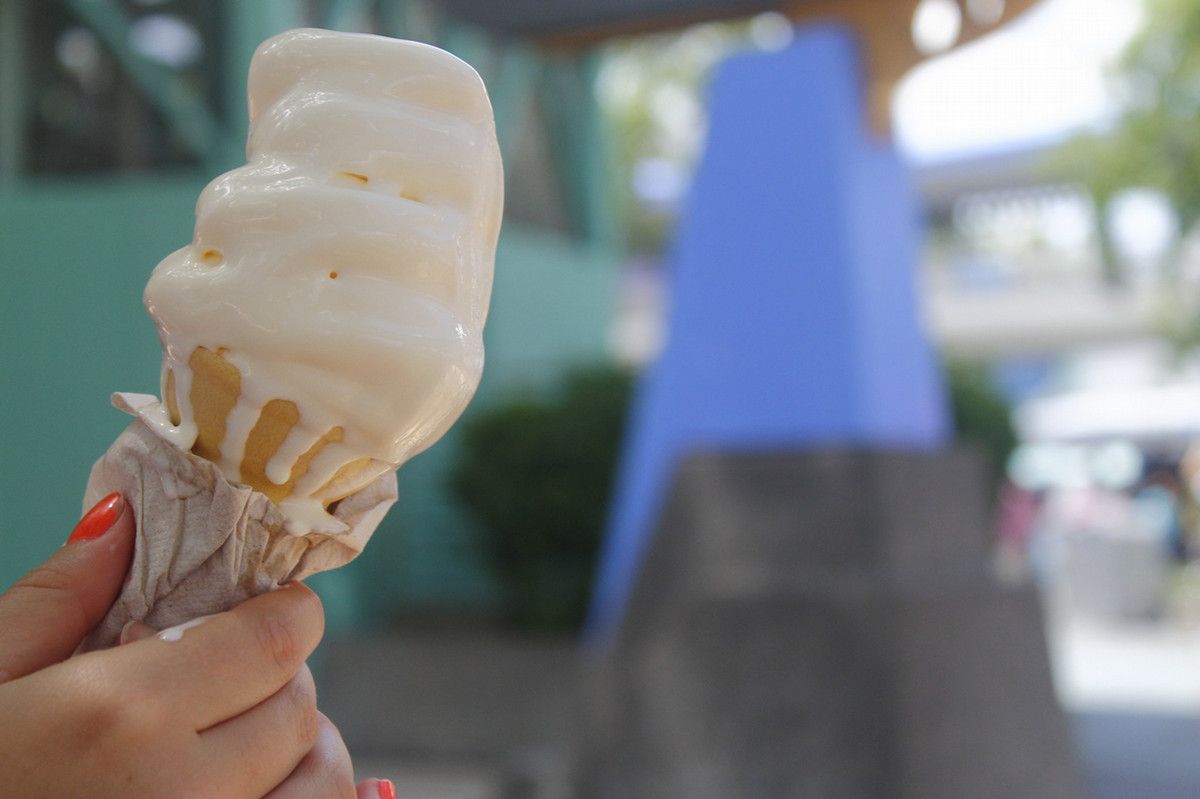 A girl holding a melting vanilla ice cream cone out in the sun