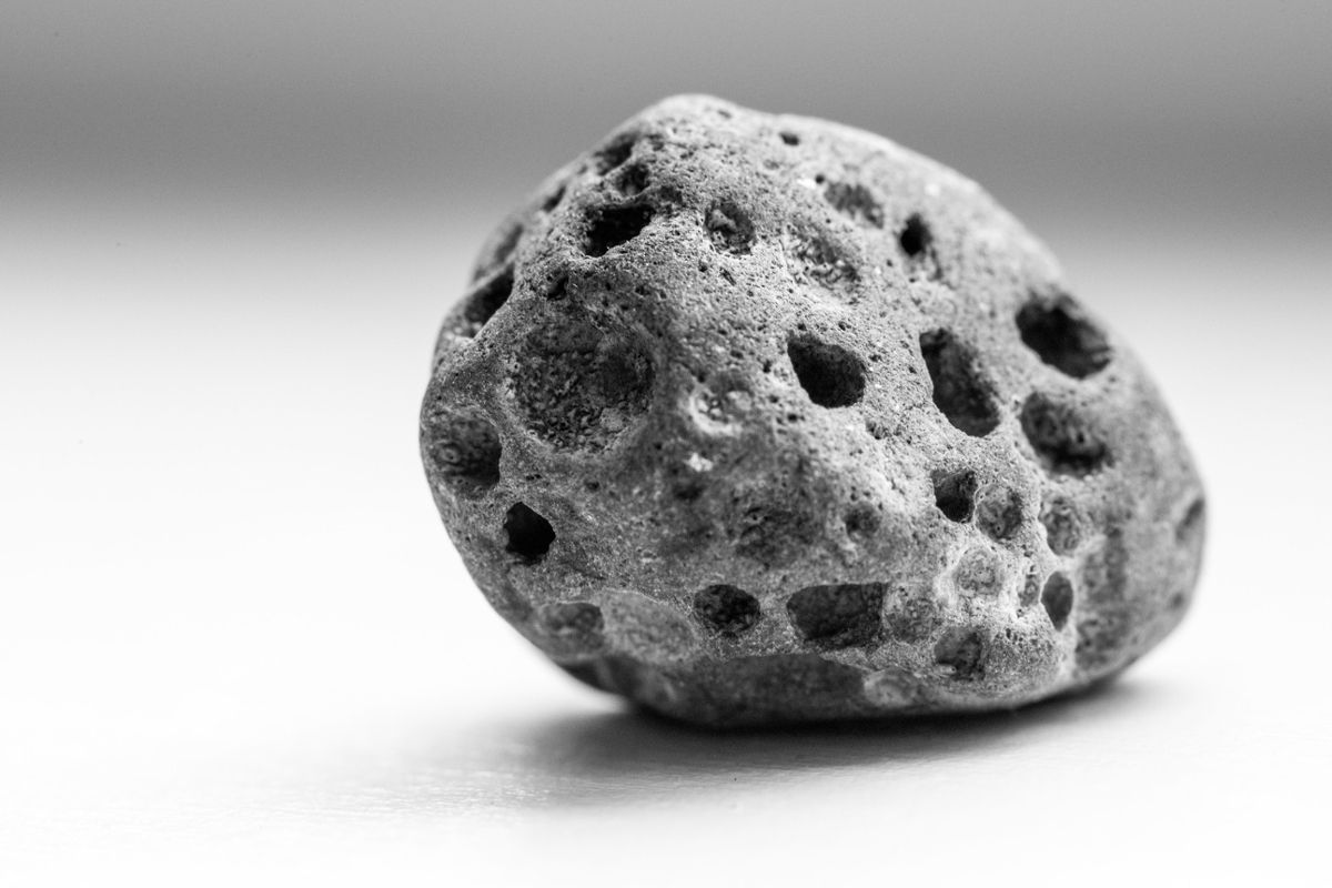 A pock-marked meteorite on a white background by itself