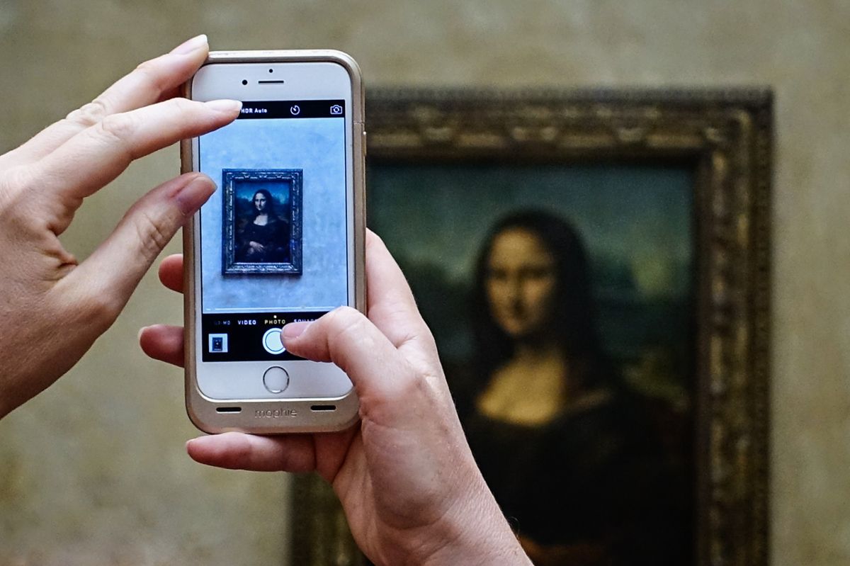 Someone taking a photo of the Mona Lisa painting on their smart phone