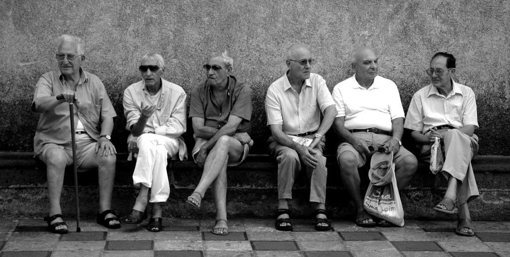 A group of older men all sitting and talking together, in black and white