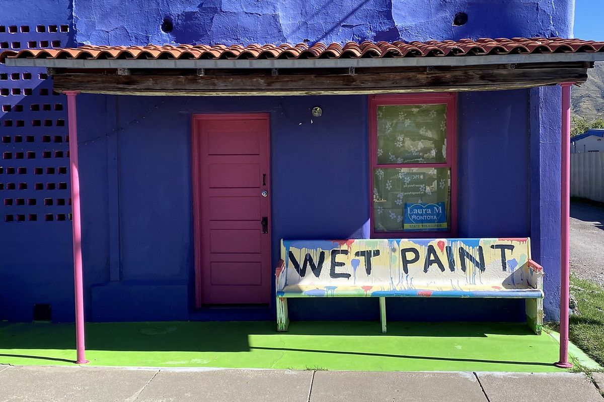 A bench that reads "wet paint" in front of a colorful, purple house with a pink door