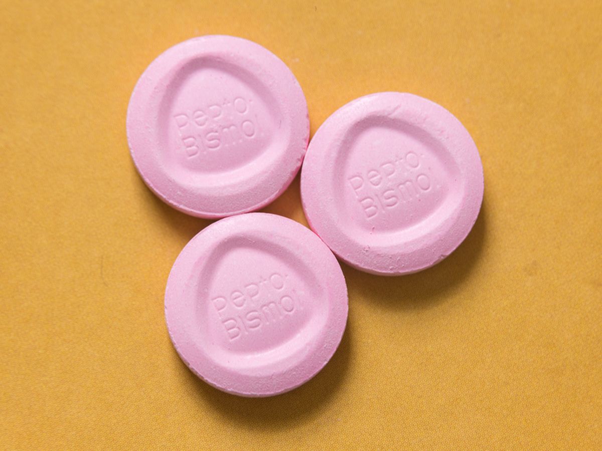 Three circular Pepto Bismol tablets against a tan background