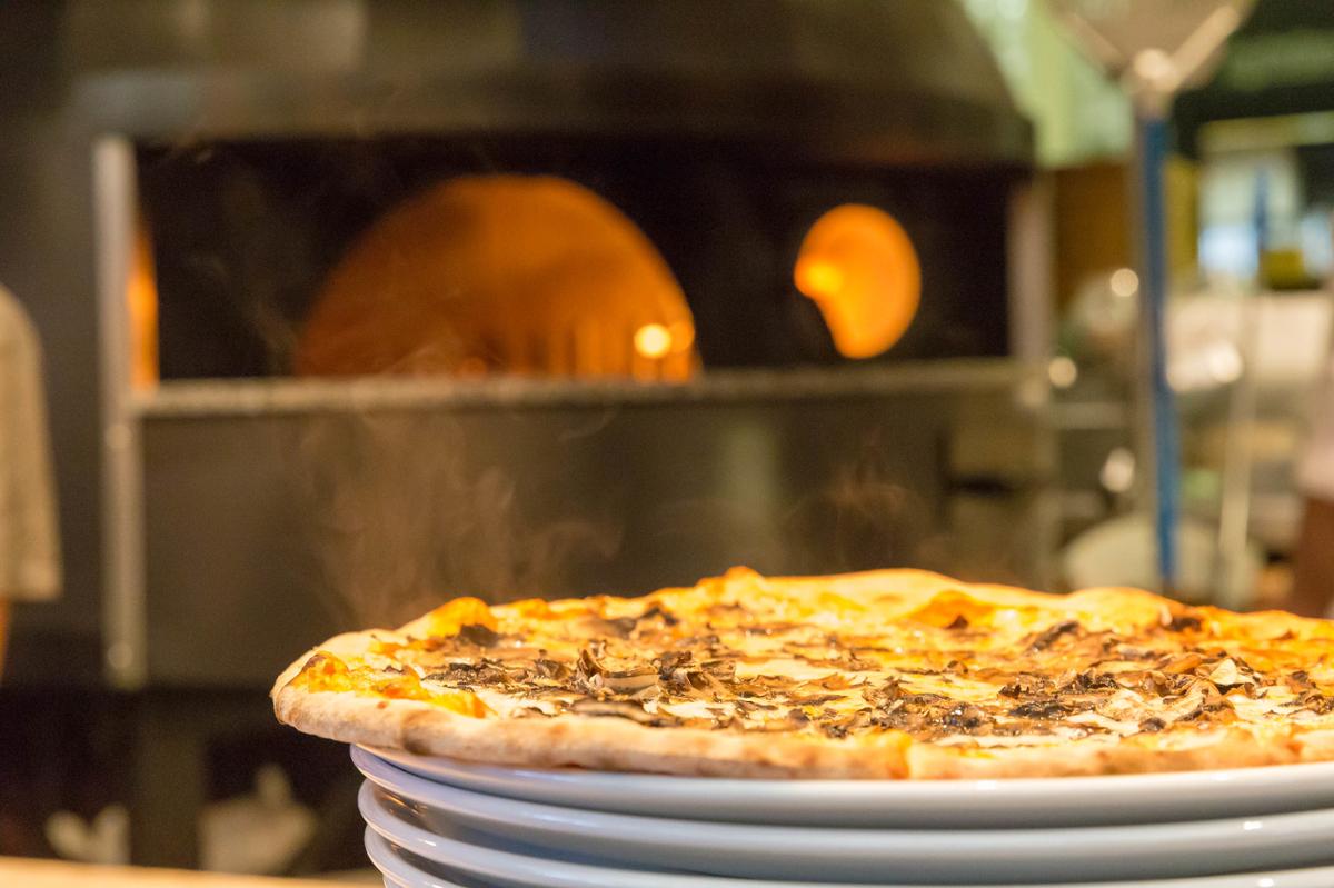 A pizza with mushrooms is steaming on a stack of plates with a hot pizza oven out of focus behind it