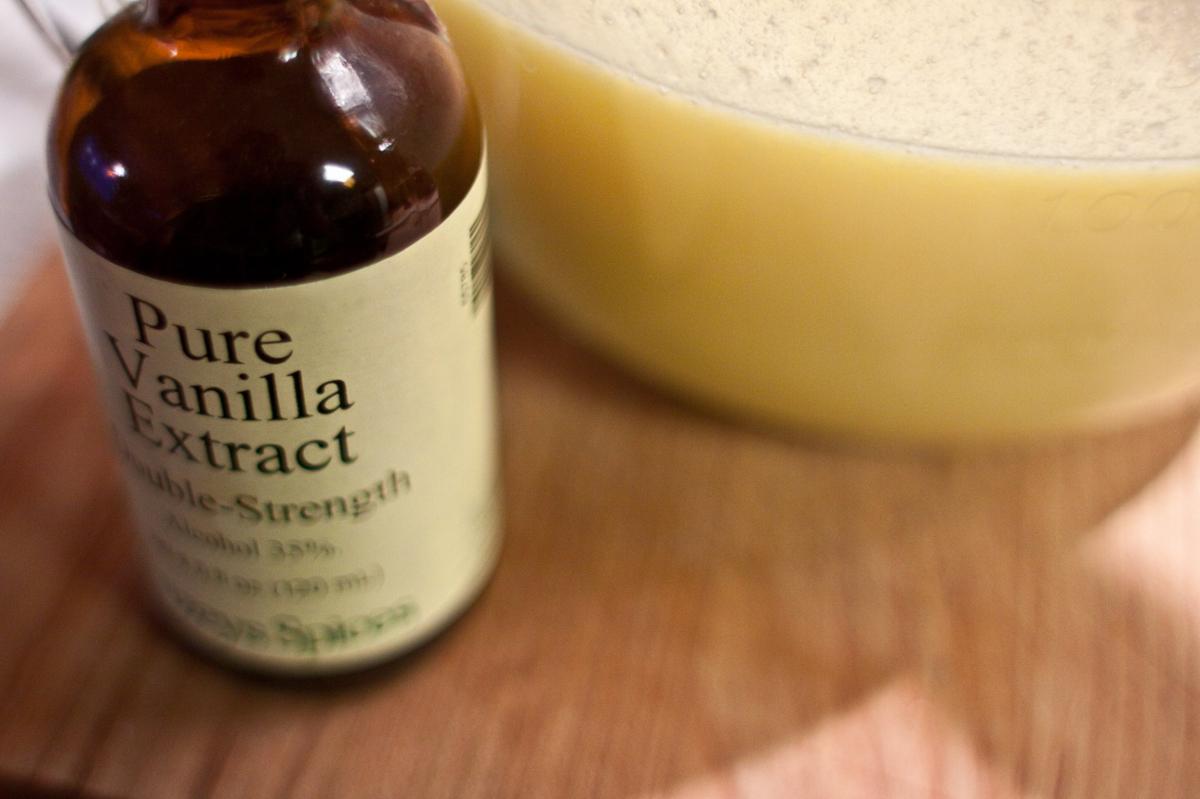 A bottle of pure vanilla extract on a kitchen counter with a bowl slightly out of focus