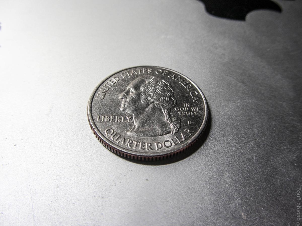 An American quarter rests on a silver metallic surface with the George Washington side faceup