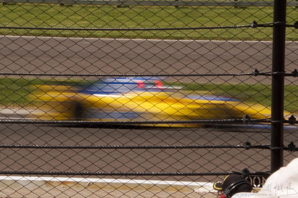 A yellow racecar speeds by the camera in a blur