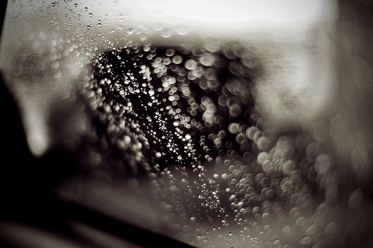 A black and white closeup of raindrops on a car's window