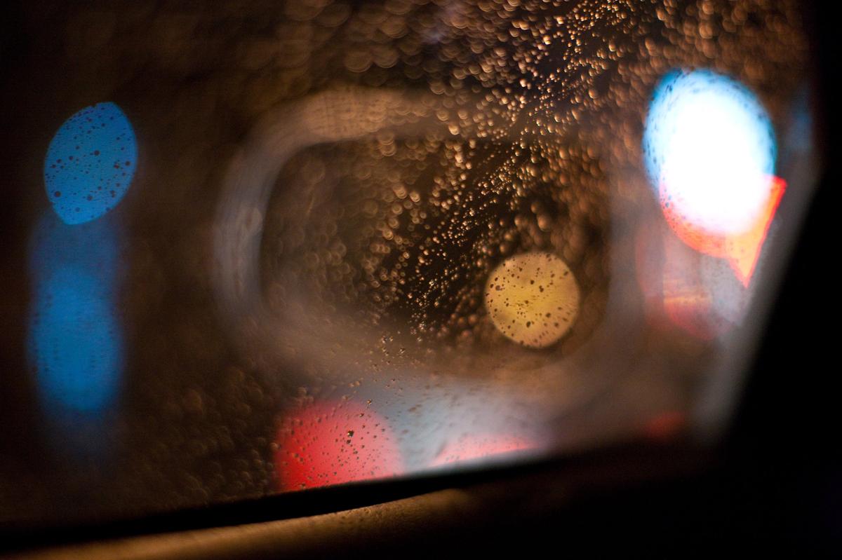 Raindrops on a window pane inside of a car with city lights reflecting off