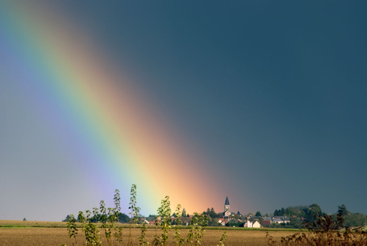 A rainbow over a small town in the distance with a blue sky