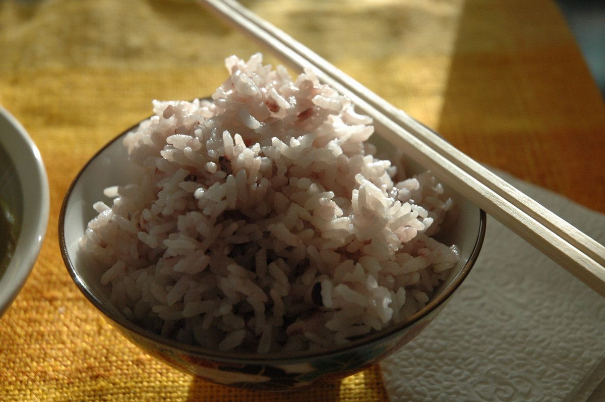 A bowl of rice with chopsticks resting on the bowl edge, partially in the sunlight on a table