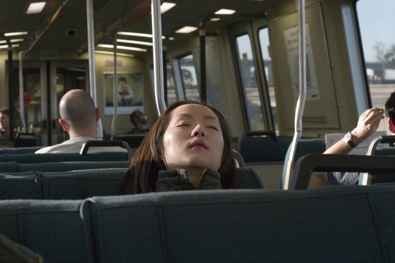 A woman sleeps with her head resting on the back of a bus seat