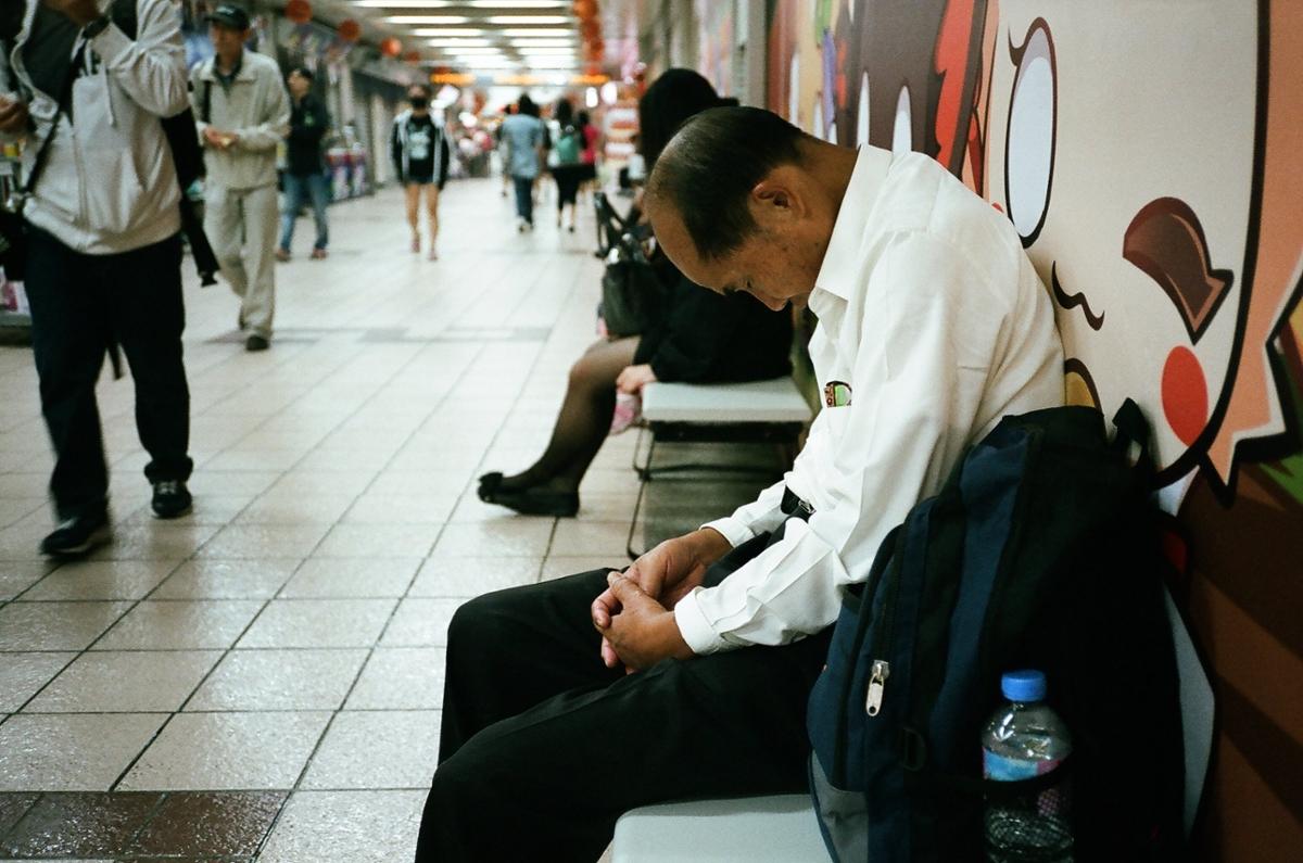 A man falls asleep on a bench in an underground subway stop