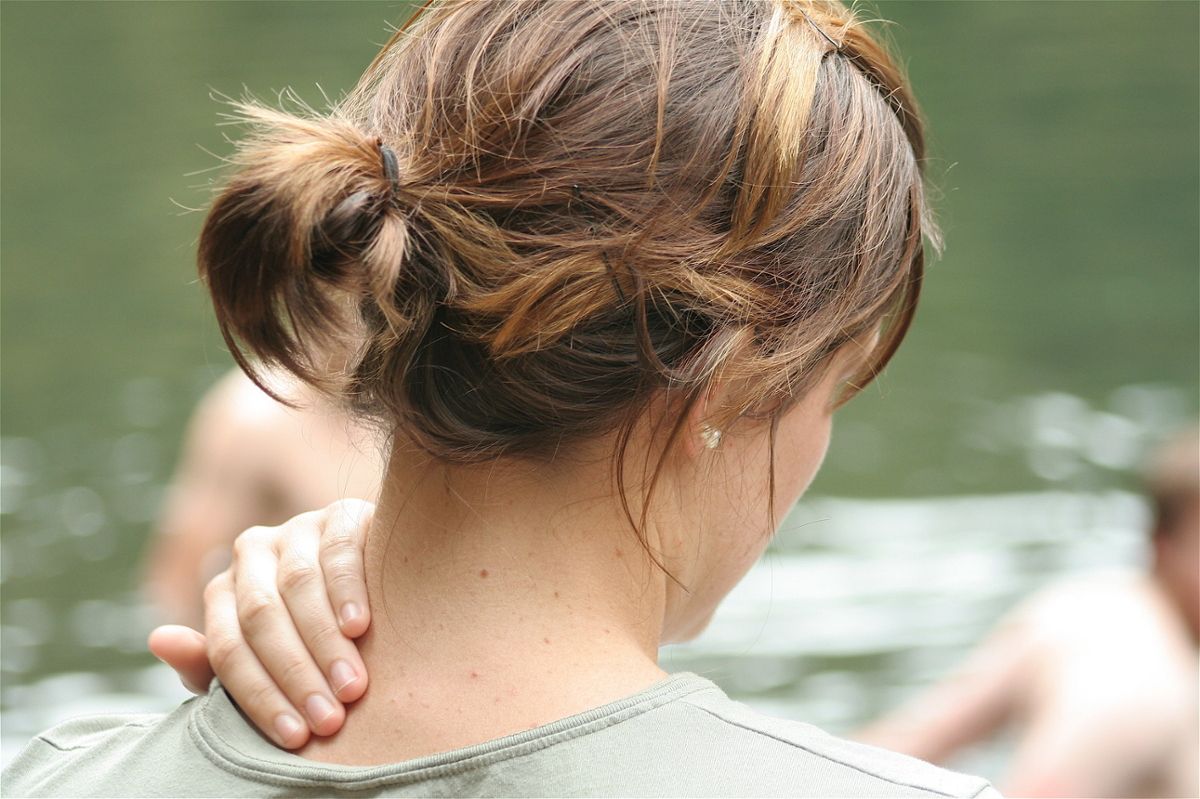 A woman with her hair up rubs the back of her neck