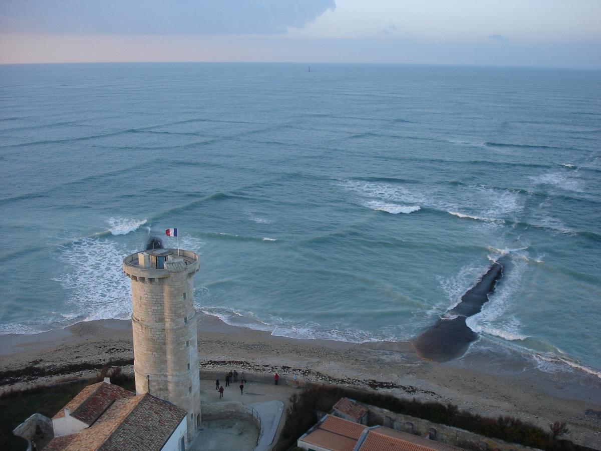 The unique wave formation off of France, square waves in the water with a view of a tan lighthouse