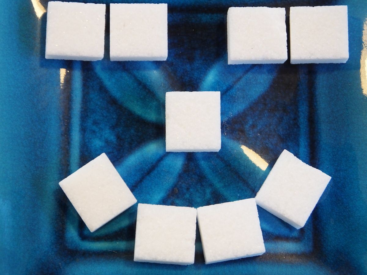Nine sugar cubes arranged to make a smiling face on a blue tiled surface