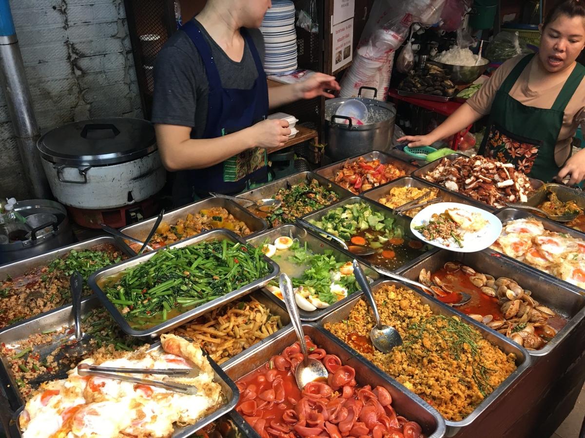Two women in aprons help prepare a colorful selection of various Thai foods in Bangkok
