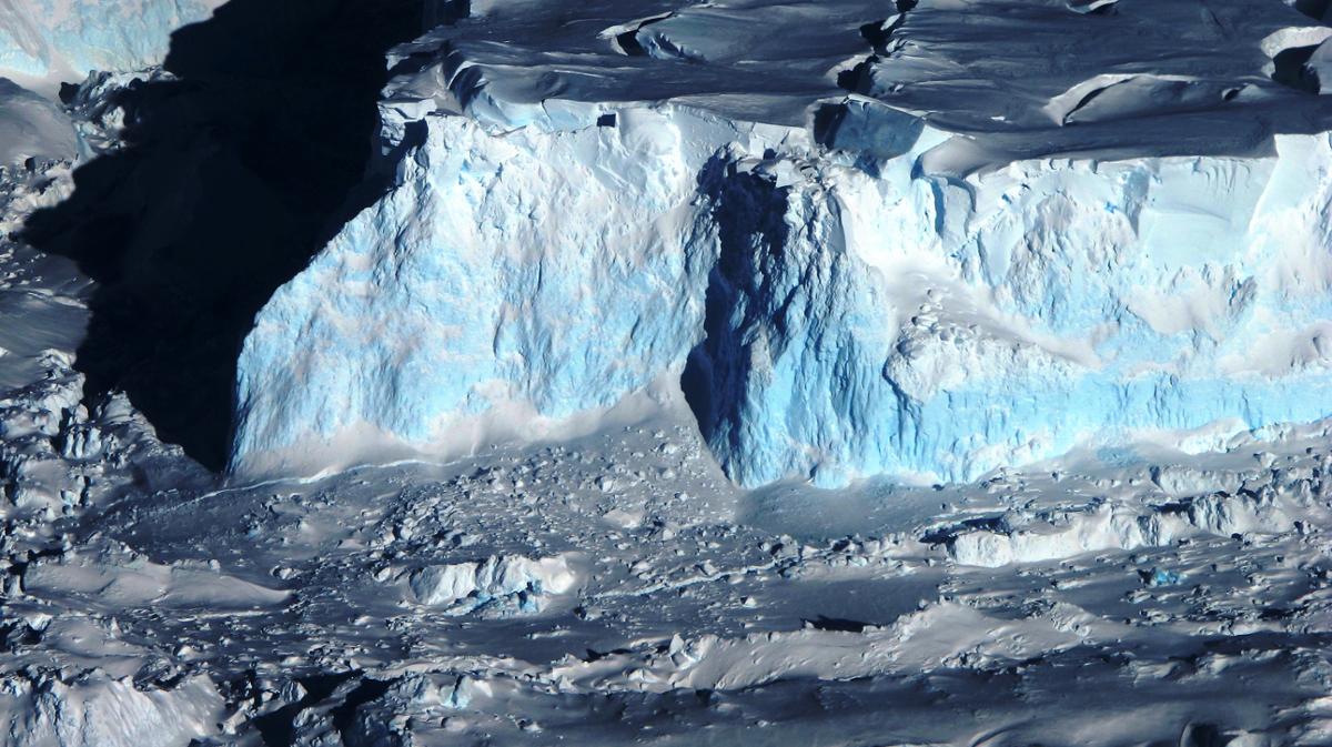 An aerial photo of a very tall glacier in Antarctica, with patches of blue ice