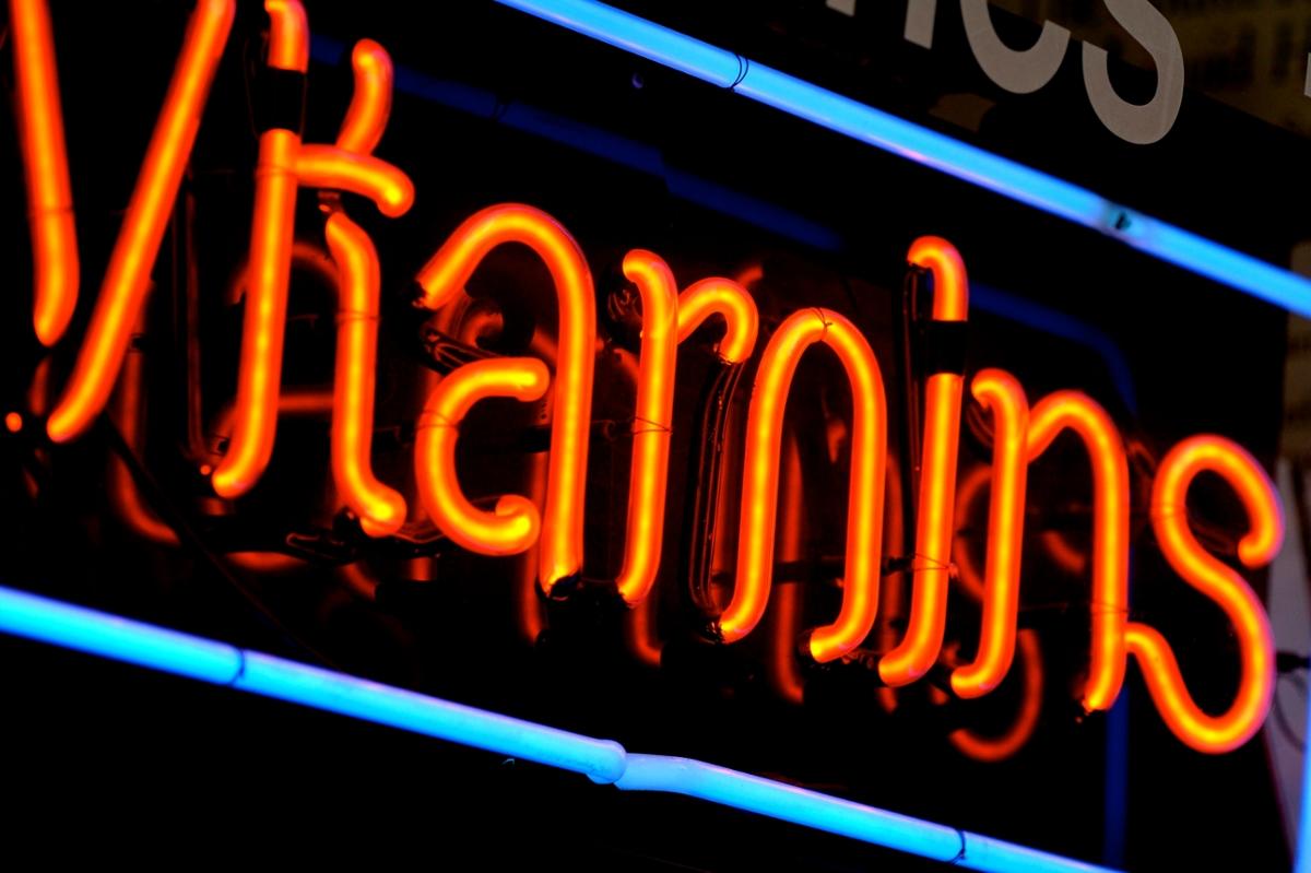 An orange neon sign for vitamins with a blue neon border
