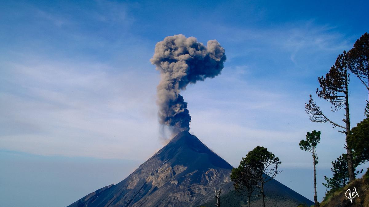 A volcano in Guatemala erupts with smoke against a blue sky