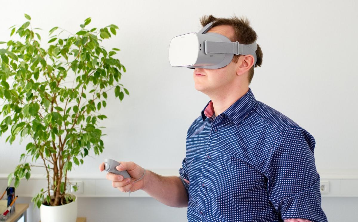 A man uses a virtual reality headset in a bright white room with a tree in the background