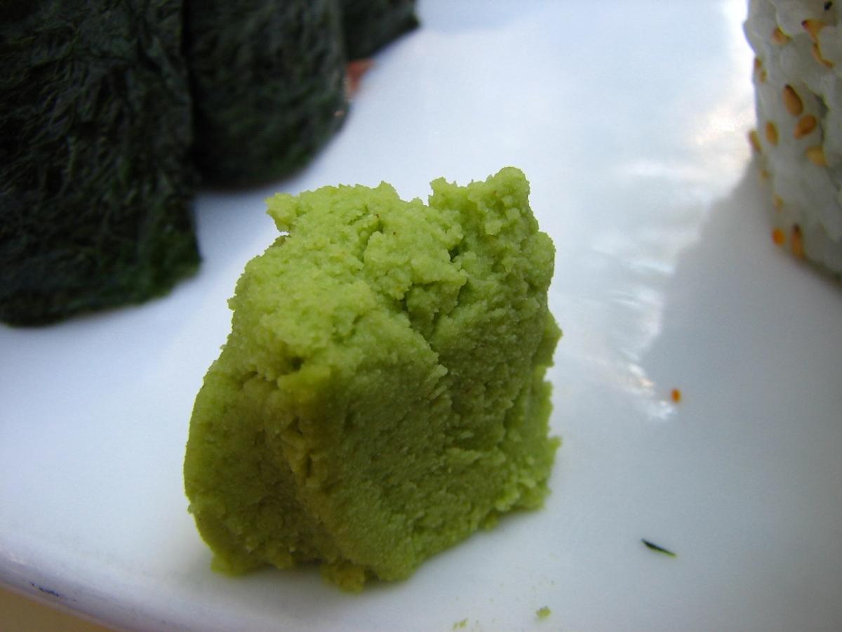 A mound of wasabi paste on a white plate, next to sushi rolls