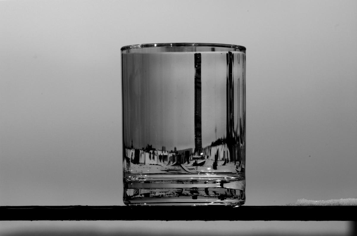 A clear glass of water distorts surrounding reflections, in black and white