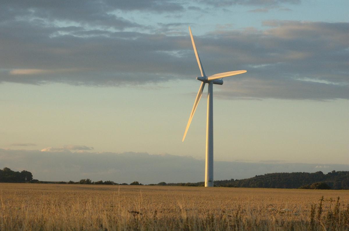 A lone wind turbine stands in a tan field facing a sunset