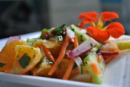 Close up of salad, with citrus and carrot, glossy with dressing, an orange flower on the plate