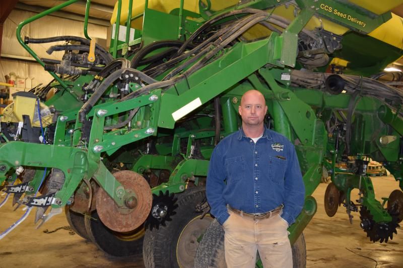 Kelly Garrett standing in front of a large green piece of heavy farm equipment.