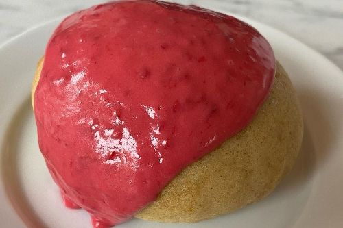 A spherical baked good with a bright pink icing draped over most of it