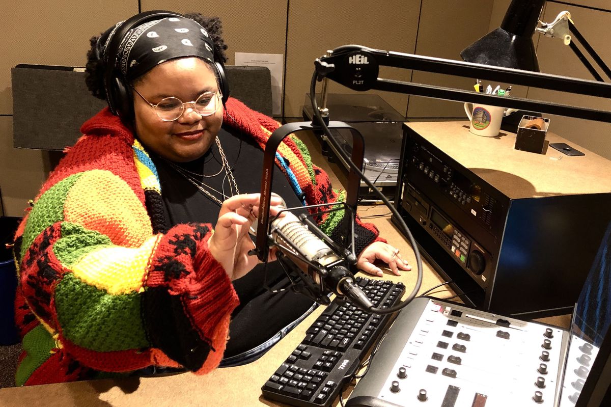 Daniella Richardson with headphones on, sitting at desk with mic and mixing board