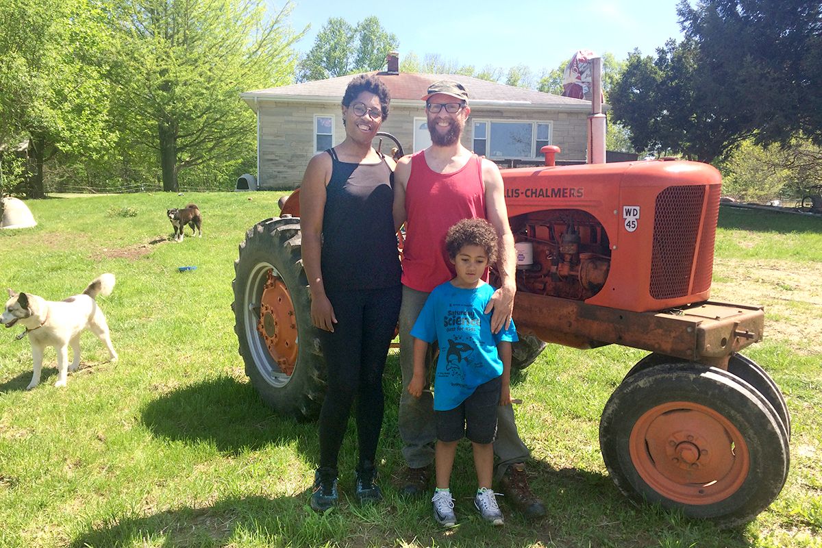 Lauren, Brett and Jasper in front of an old red tractor with limestone house in background and 2 dogs