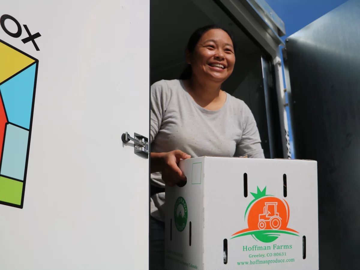 Women in a doorway holding a white cardboard box of produce