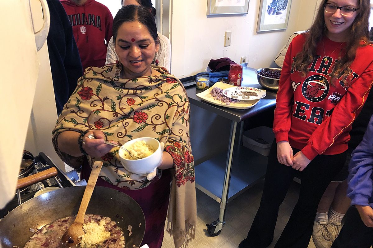 Kashika Singh standing at stove with a bowl of chopped ginger while other people look on
