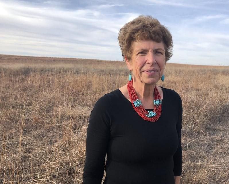 Mary Chris Barth standing in a field of brown grass, with a flat, uninterrupted horizon and gray blue sky 