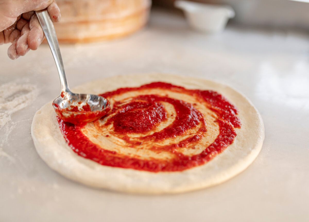 Marinara being spread on pizza dough