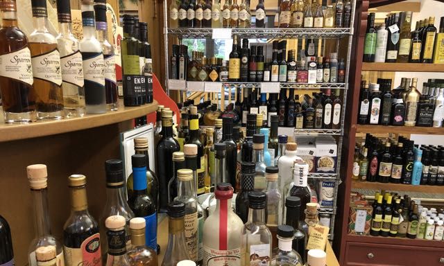 many different bottles of vinegar and oil arranged on a bar, with shelves of bottles in the background