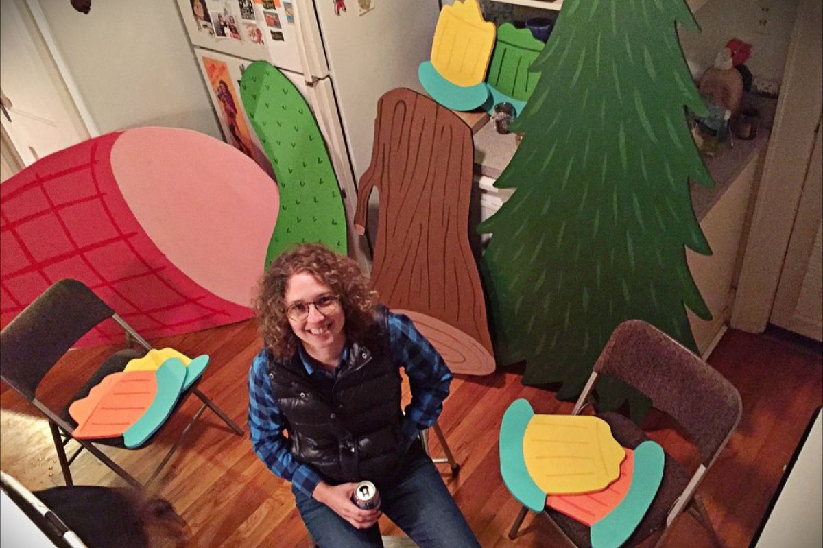 View from above of Emily Wallace siting on a chair looking up, surrounded by large illustrated foods like a ham and a pickle