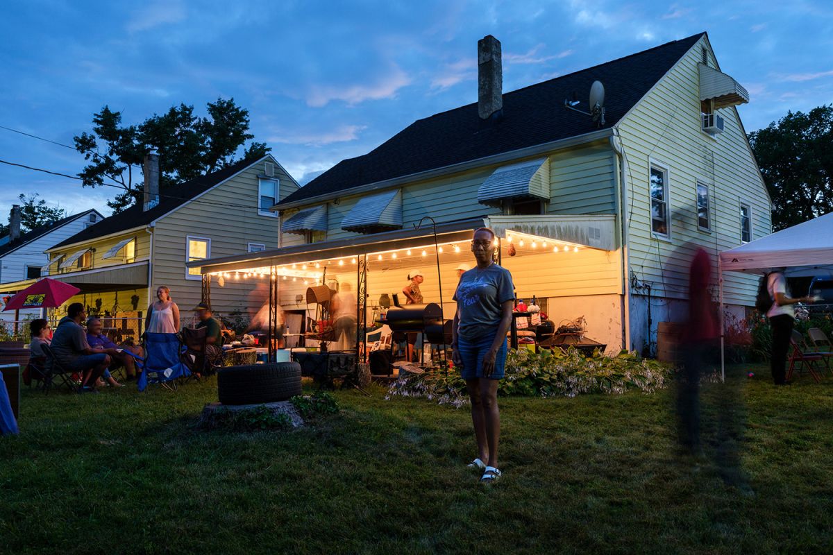 A woman stands in a yard with a cookout in the background