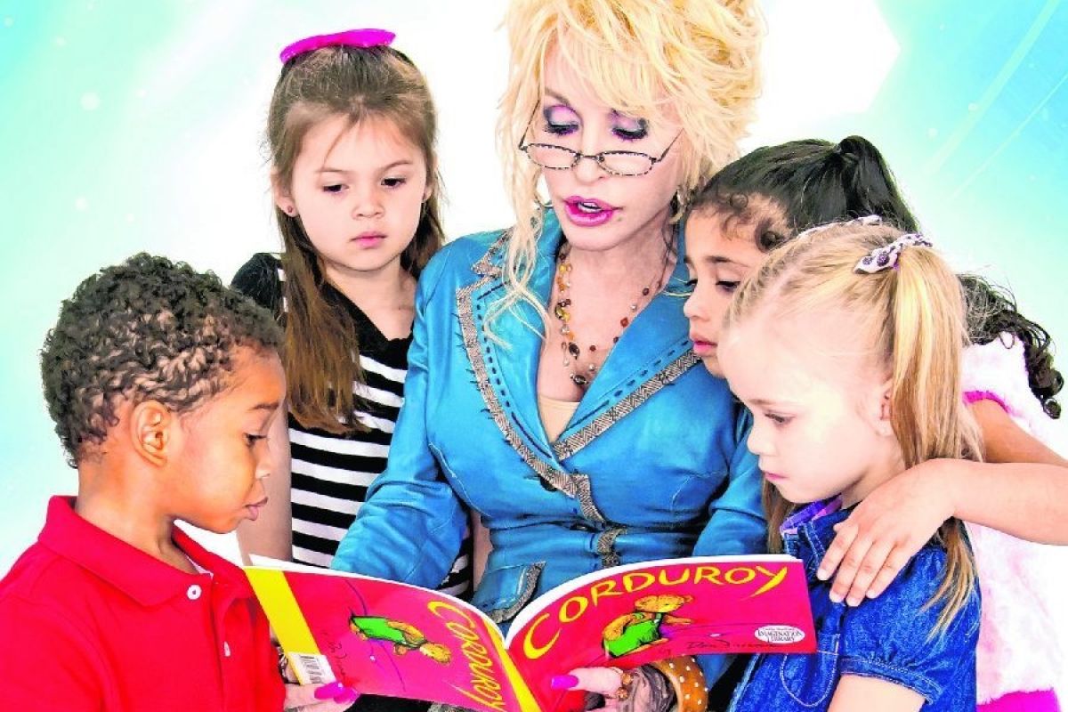 Dolly Parton sits and reads a book to four young children.