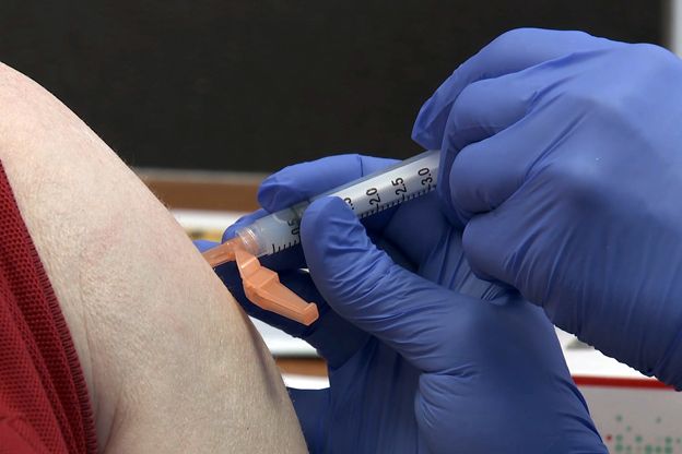 Image of gloved hands administering a COVID-19 vaccine in a persons arm.
