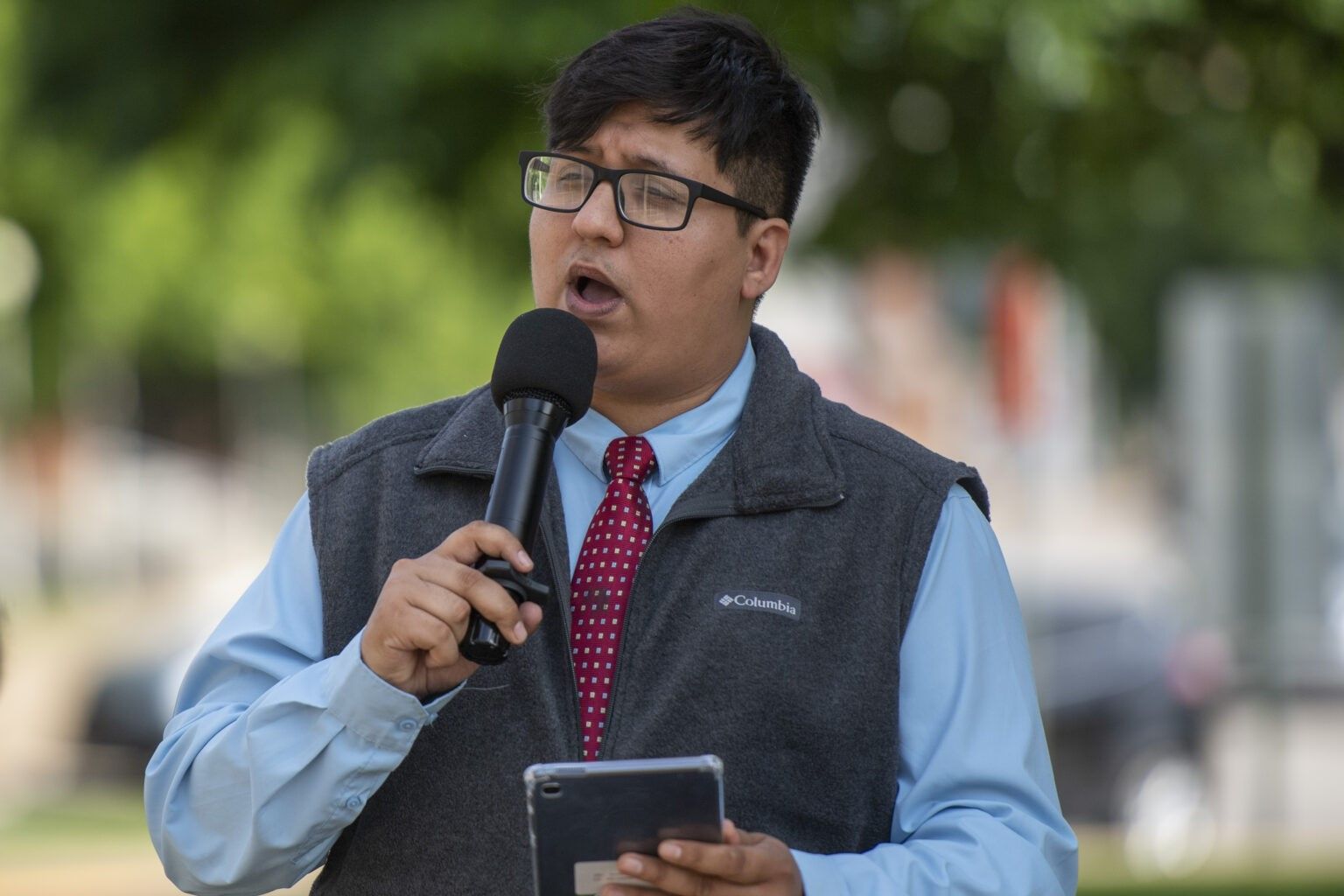 Gabe Whitley speaking into a microphone while holding a tablet at a rally