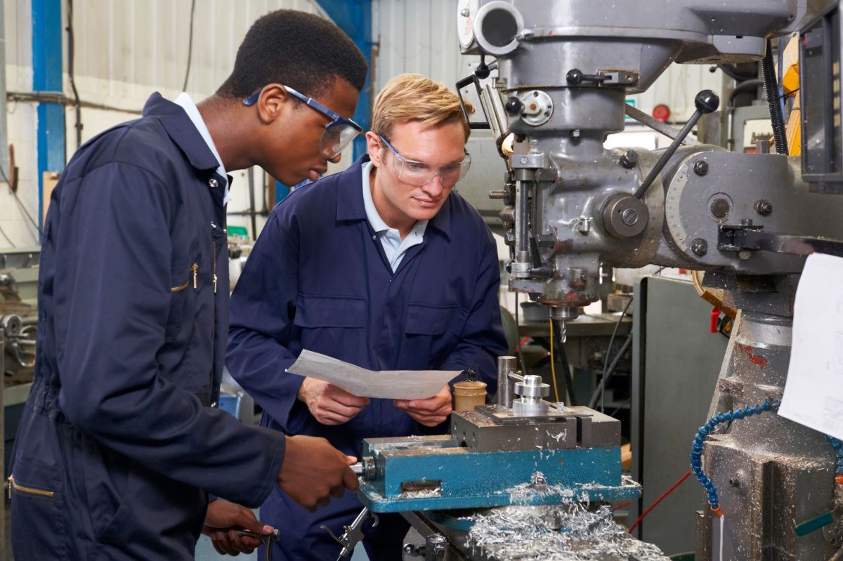 Engineer Showing Apprentice How to Use Drill In Factory