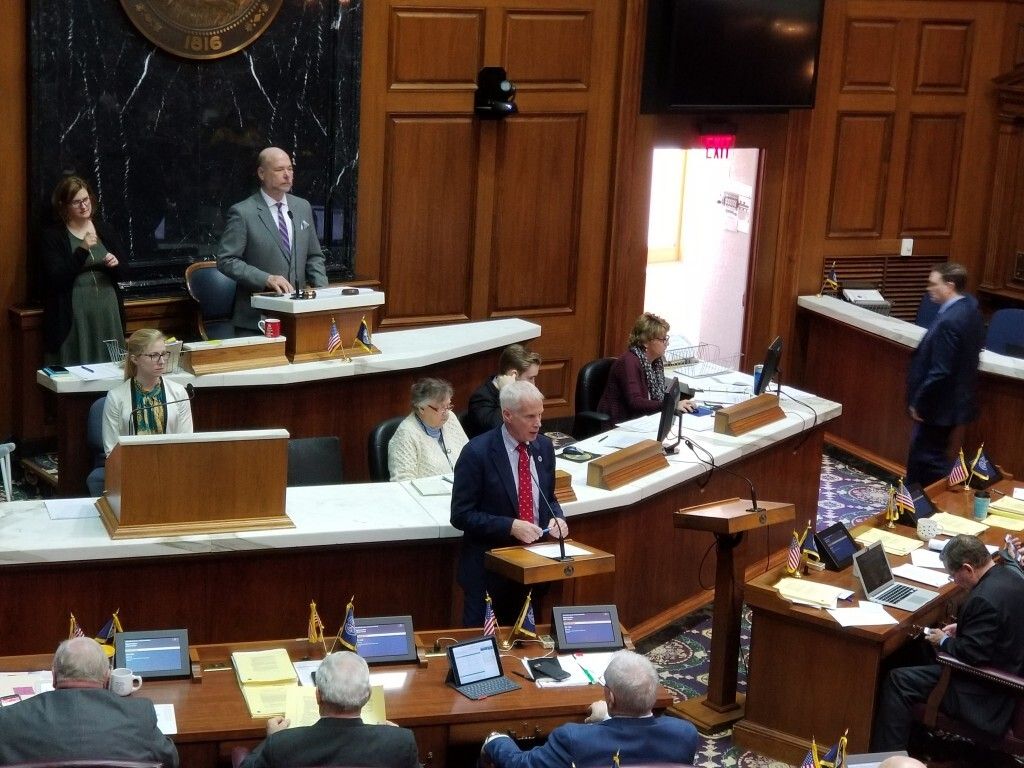 Bob Behning stands at a podium in the Indiana House Chamber.