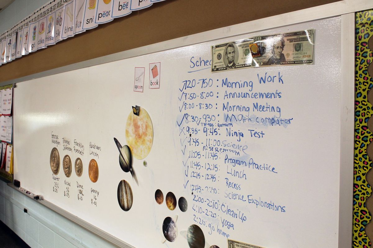 The whiteboard of an elementary school classroom lists the agenda for students along with magnets displaying currency and their values.