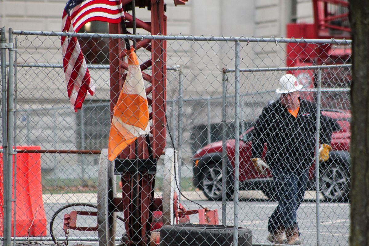 A worker walks outside of a wire fence along a crane in a construction site.