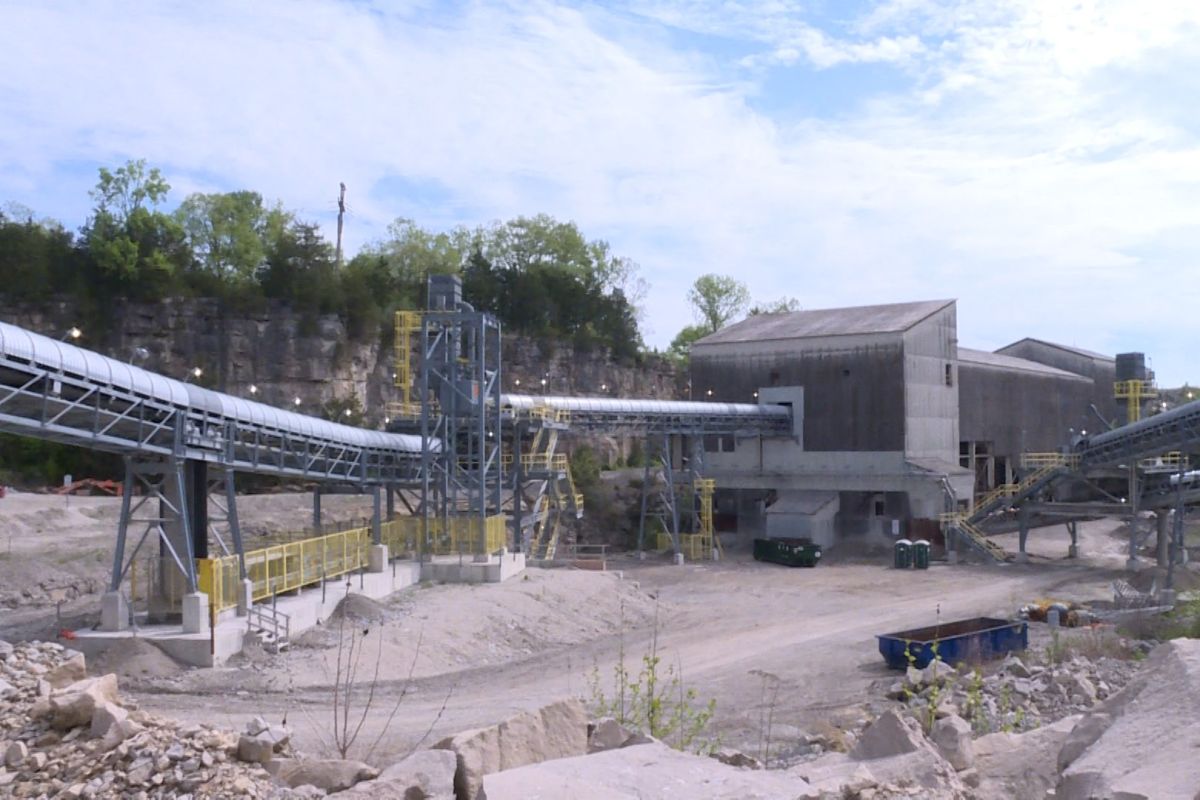 In this building at Heidelberg Materials in Mitchell, limestone is crushed to be used in cement making. Covered, steel tracks feed into the upper levels of a large building. Two port-a-potties are on the ground floor, dwarfed by the building. 
