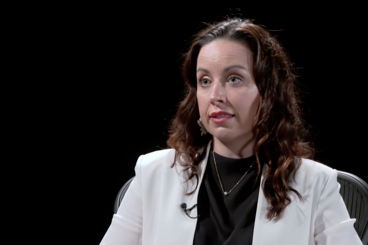 A screenshot from a video interview with Destiny Wells. Wells is a White woman with dark brown hair. She is wearing a white jacket over a black top.